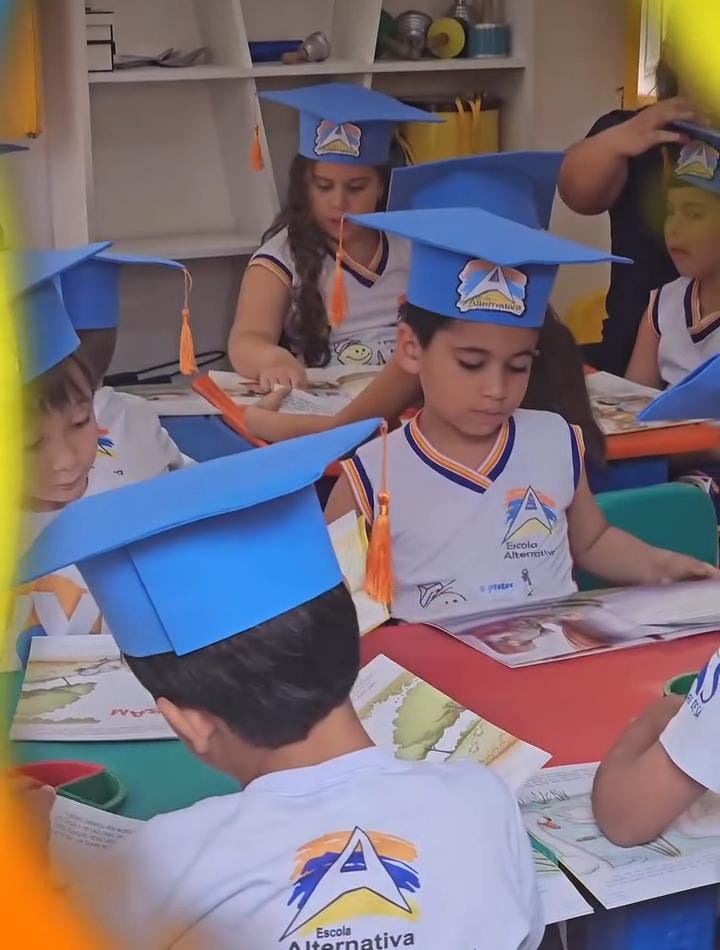 Alunos da educação infantil com capelos em atividade de leitura